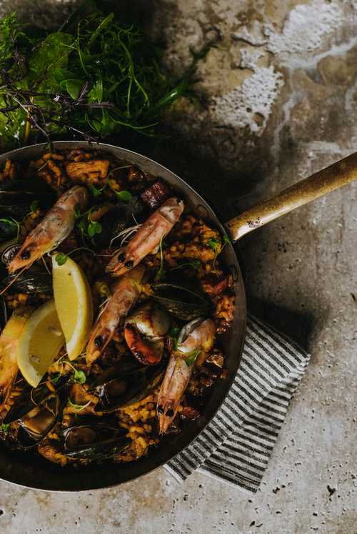 Birds eye view of paella dish with king prawns, mussels and lemon wedges